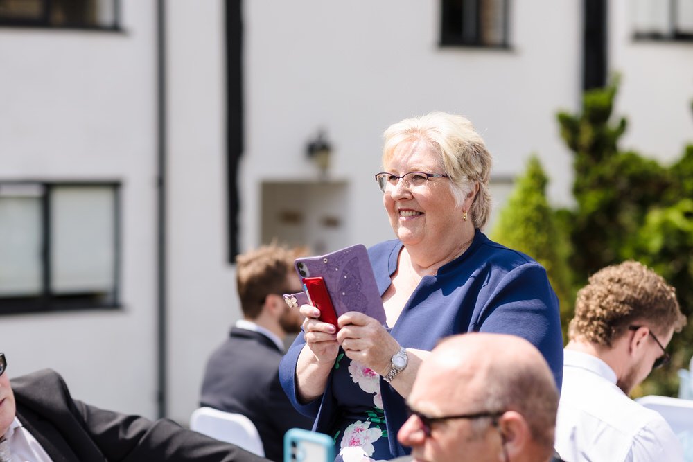 Smiling guest records the outdoor ceremony with two smartphones at Karma Salford Hall.