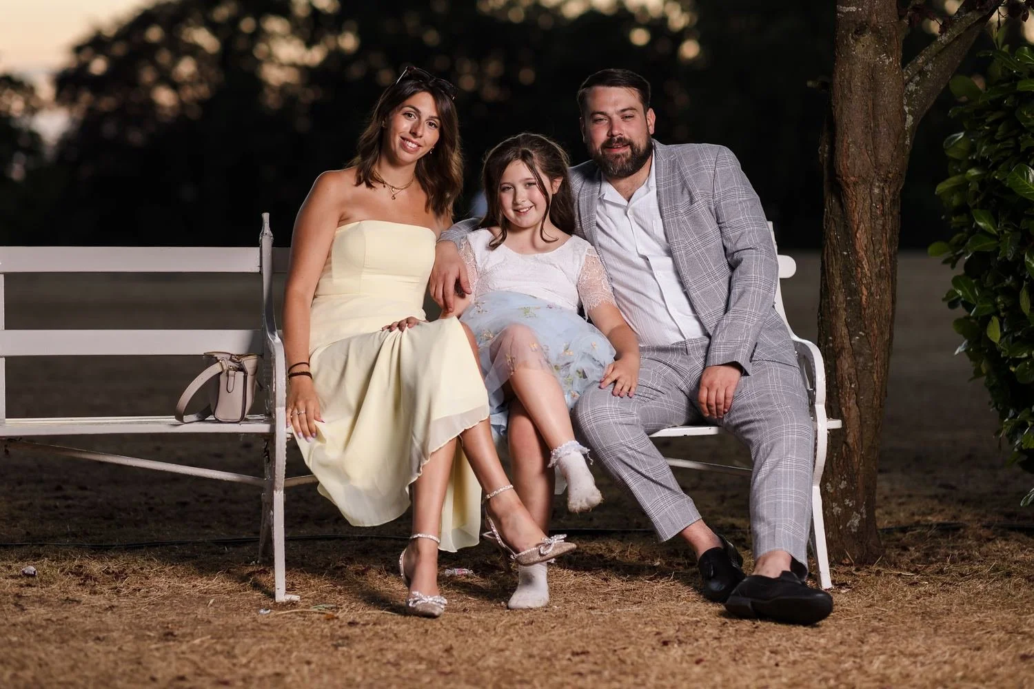 A family of wedding guests on the white garden bench at sunset, lit with a softbox