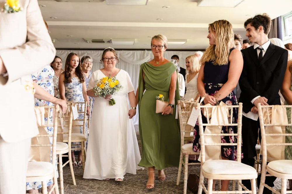 Bride walking down the aisle with her sister at a De Vere Cotswold Water Park ceremony
