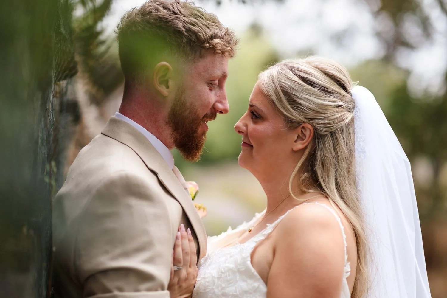 Close portrait of Abbie and Sean face to face, framed by soft green foliage in the foreground