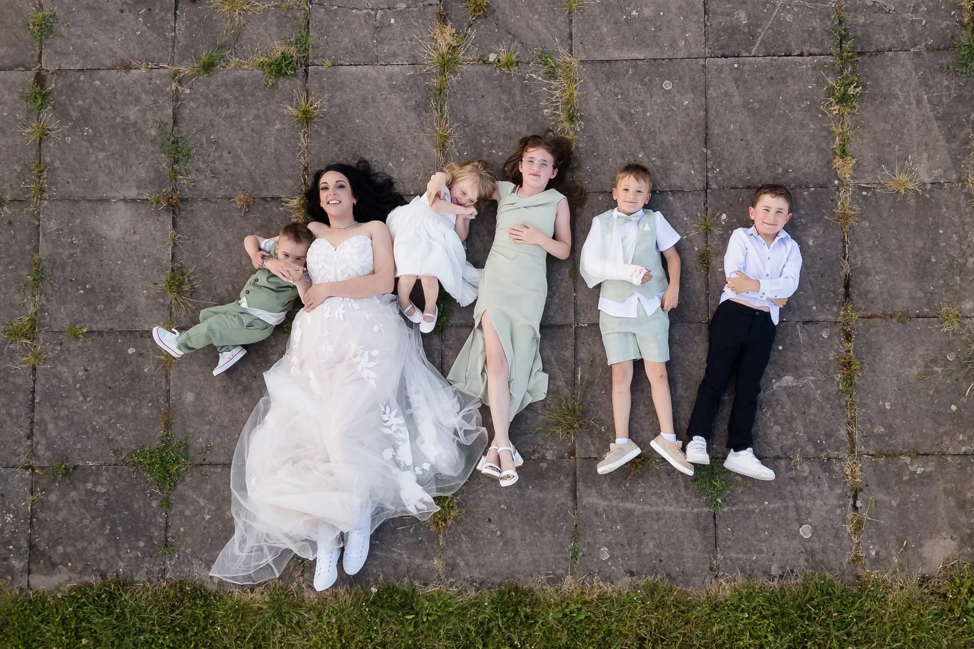 Overhead drone portrait of the bride and children lying on paving, a creative wedding photography shot in Worcestershire.