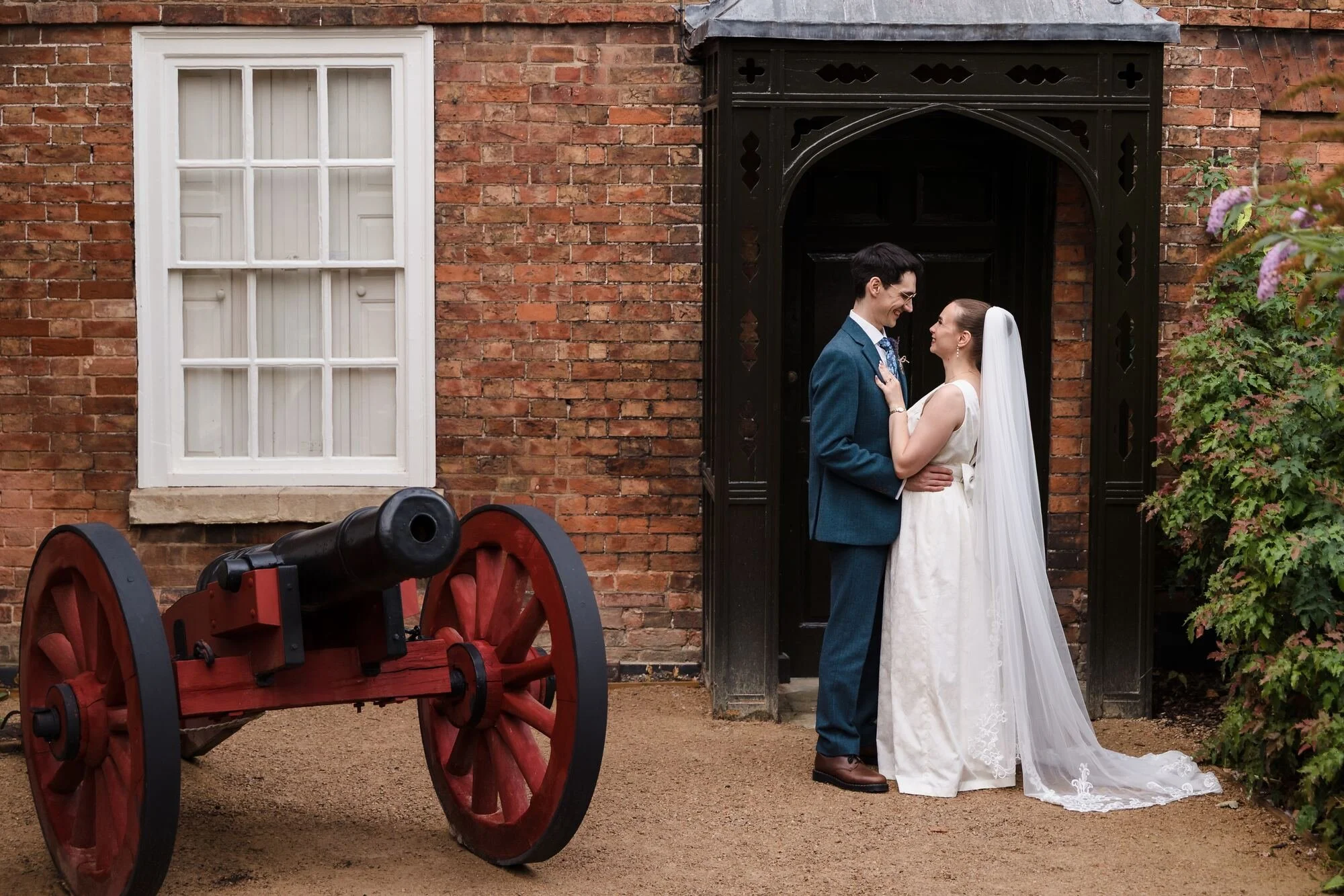 Isabelle and Chris embracing in a gothic doorway beside a red-wheeled cannon at The Commandery, Worcester, by Once in a Lifetime Photography