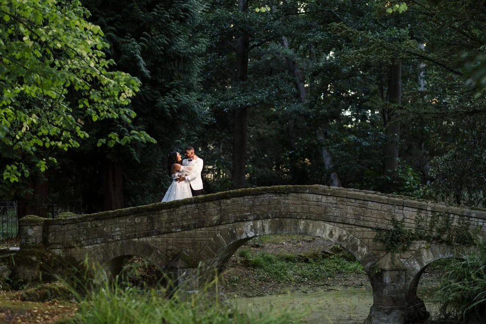 Bride and groom embracing on a stone bridge in the woodland gardens at Hogarths Hotel wedding venue.