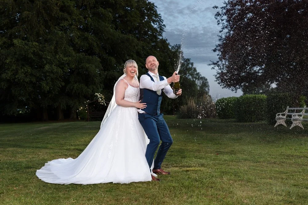 Bride and groom during a champagne spray celebration on the lawn at Hogarths Stone Manor, Worcestershire