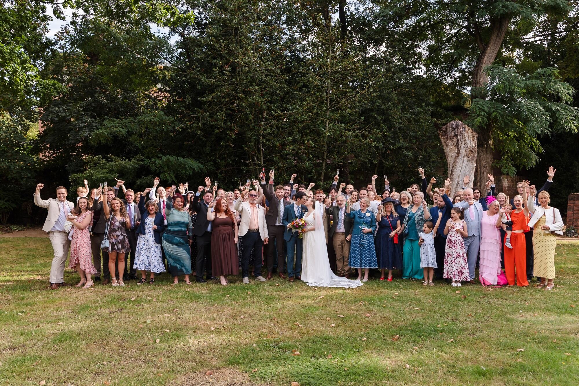 Large group photograph of cheering wedding guests on the lawn of the walled garden at The Commandery, Worcester, by Once in a Lifetime Photography