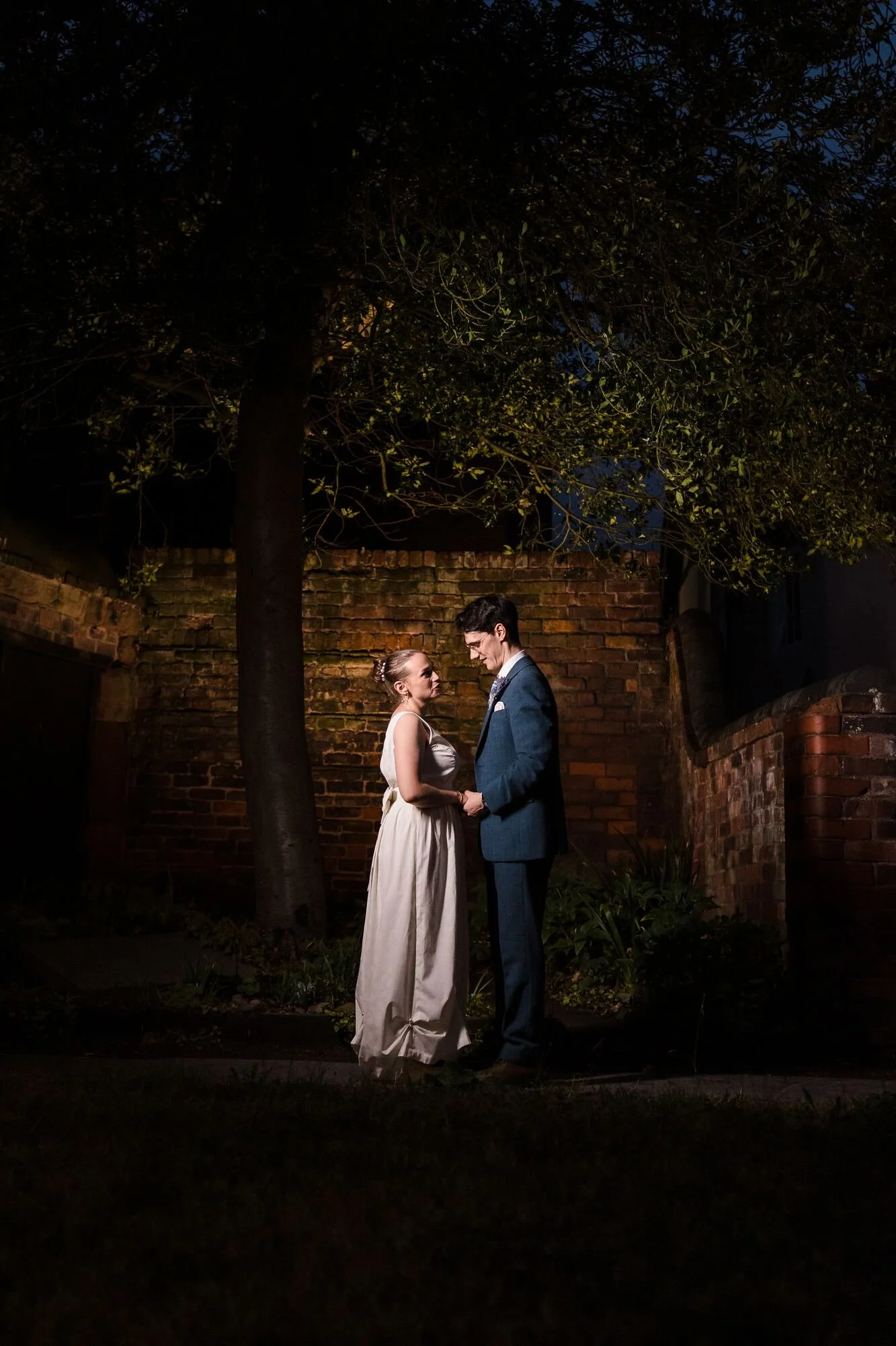 Gel-lit night portrait of Isabelle and Chris beneath a tree against the brick wall at The Commandery, Worcester, by Once in a Lifetime Photography