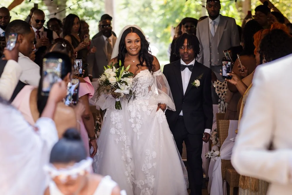 Bride walking down the aisle with her son at the outdoor island ceremony at Hogarths Hotel Solihull, guests lining both sides — candid wedding photography by Once in a Lifetime Photography, Worcestershire