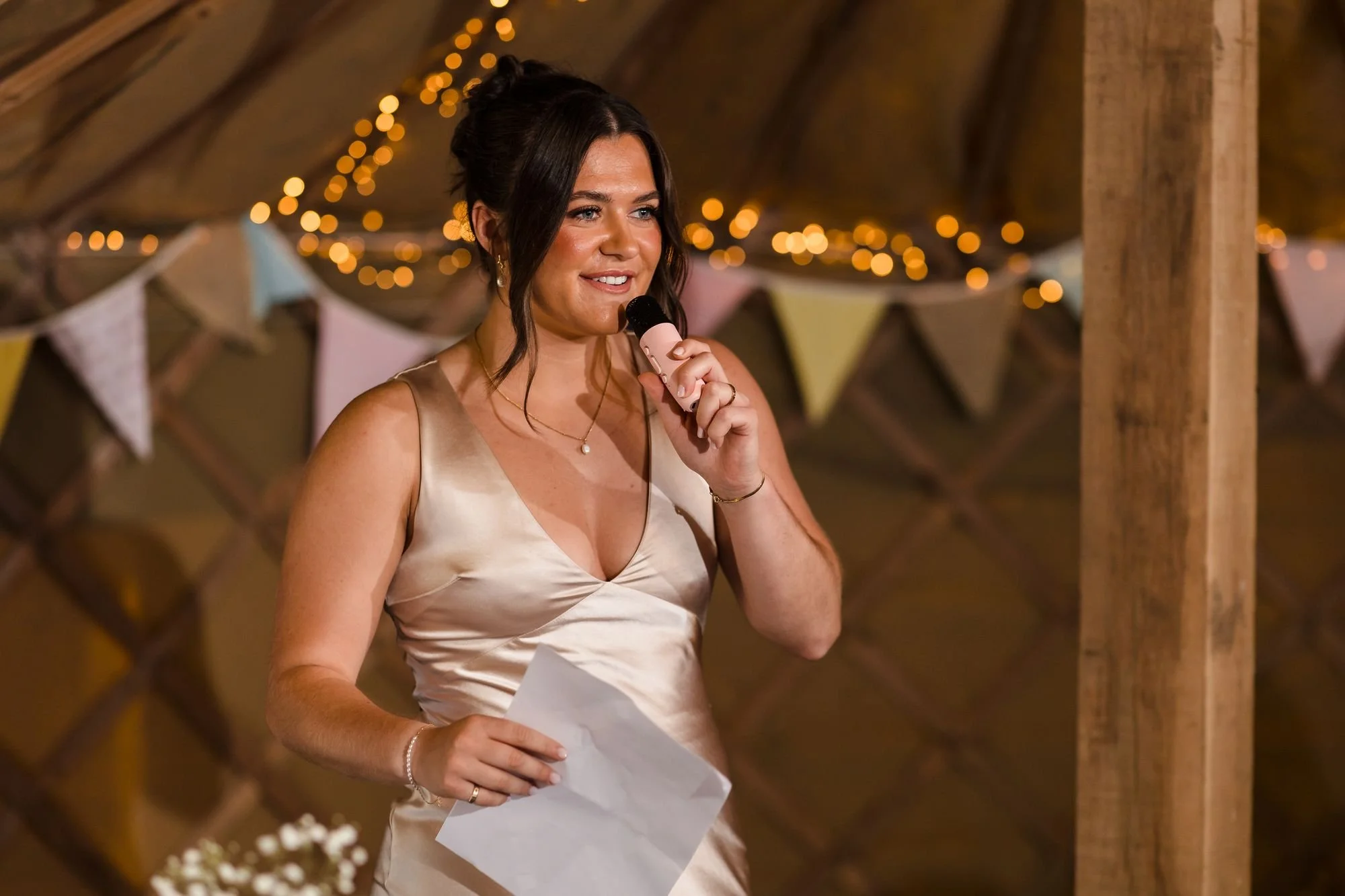 Bridesmaid smiling as she gives her speech in the Yurt Marquee, with bunting, fairy lights and lattice walls behind