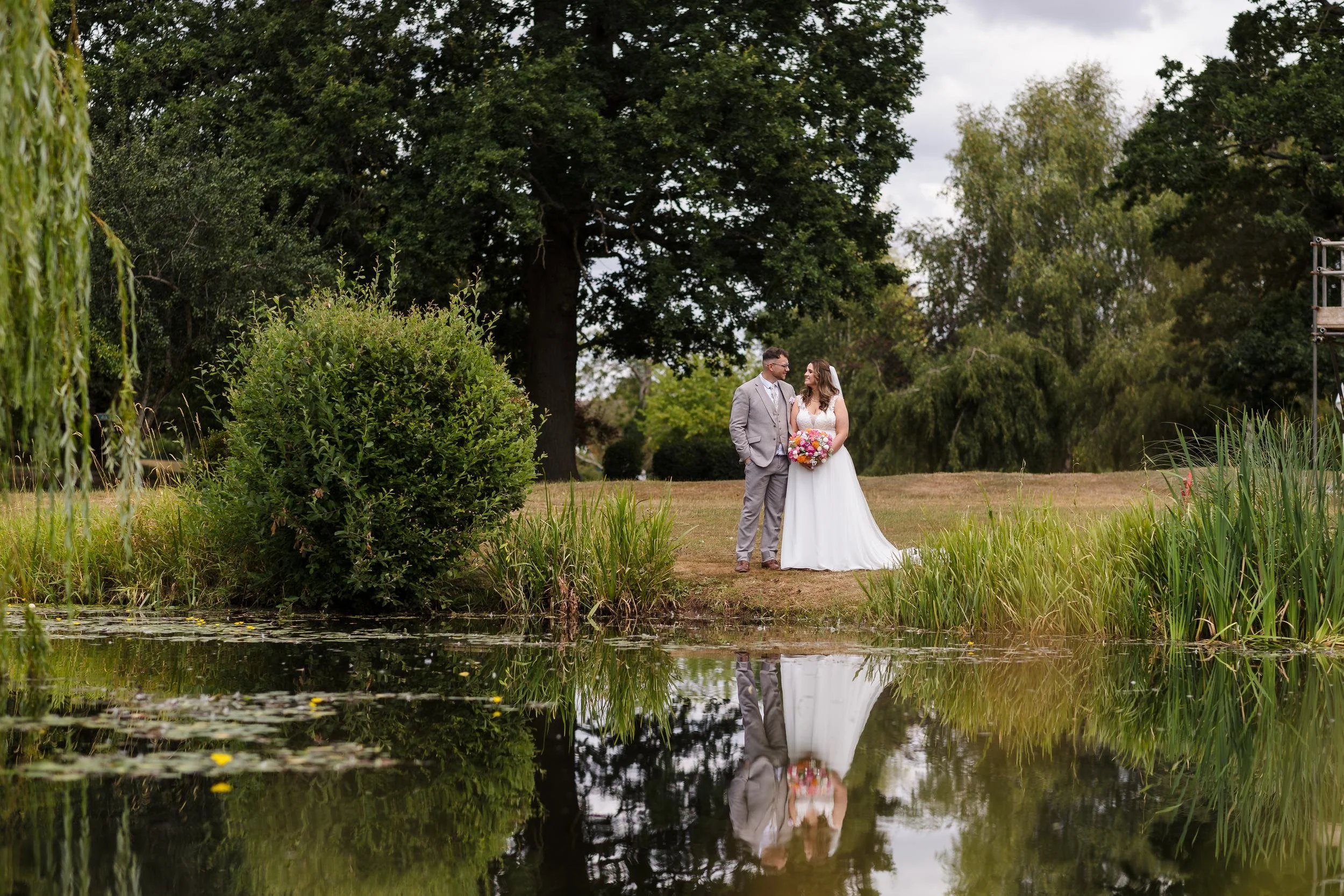 Holly and Dan standing at the edge of the lake on the Nailcote Hall golf course, reflected in the water