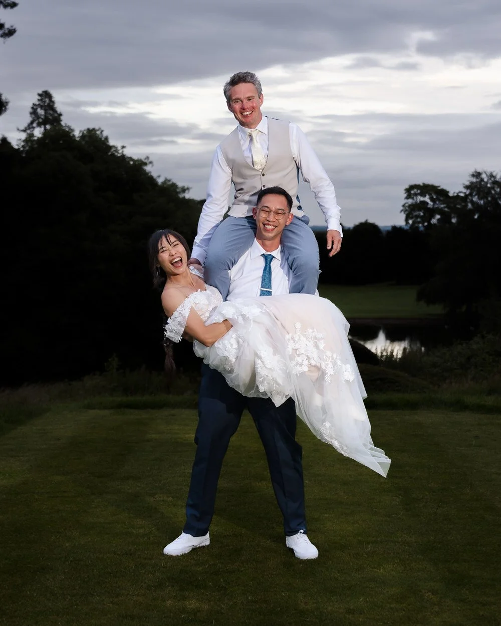 Greg carrying Christine while a groomsman balances on his shoulders, a playful evening portrait at The Welcombe Hotel.