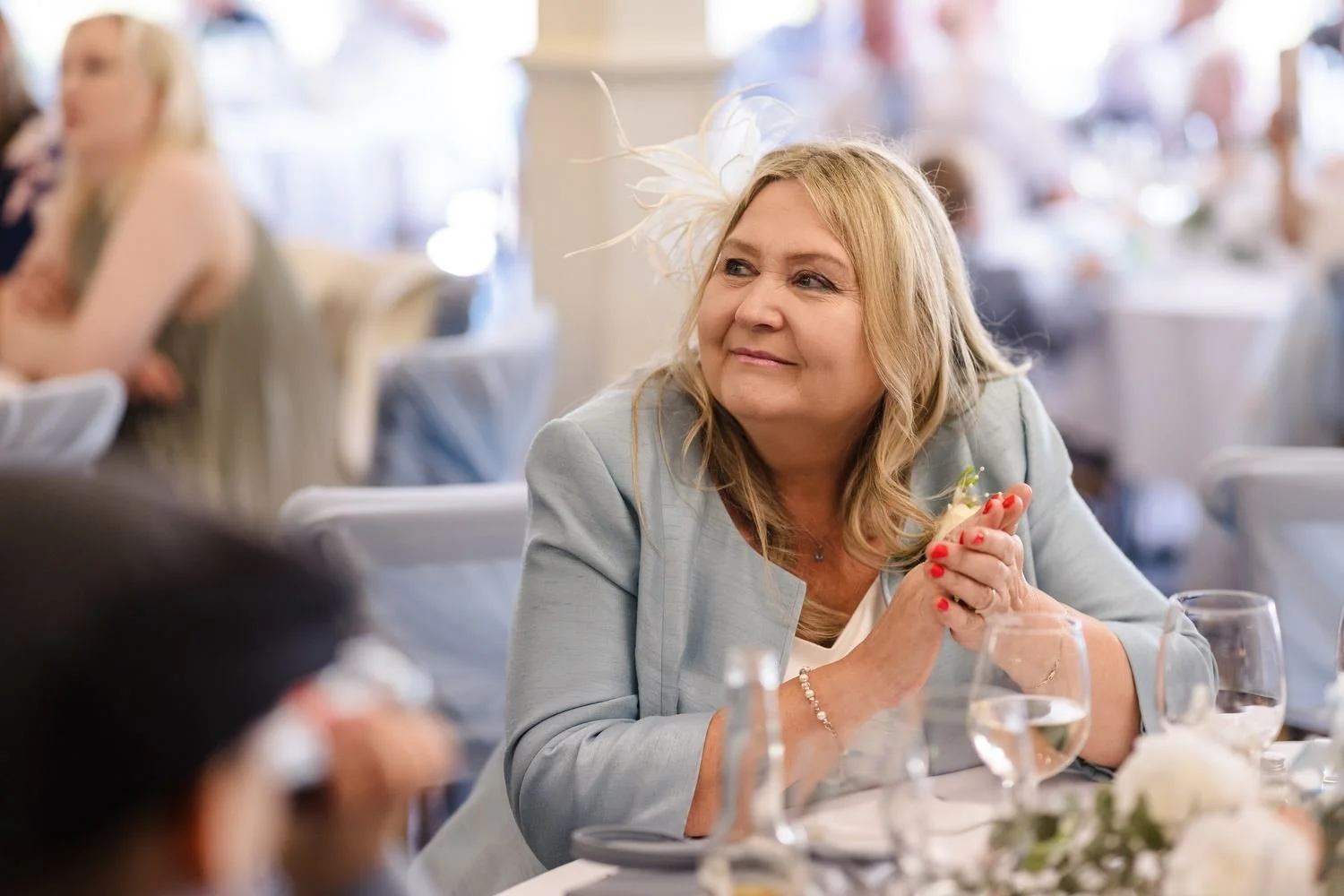 A guest in a pale blue jacket smiling as she listens to the speeches