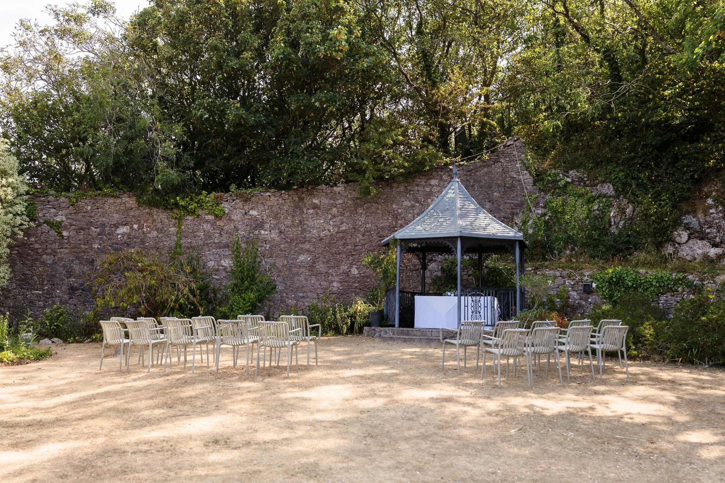 Outdoor ceremony set-up in the walled garden at Berry Head Hotel, with chairs facing the gazebo and stone wall