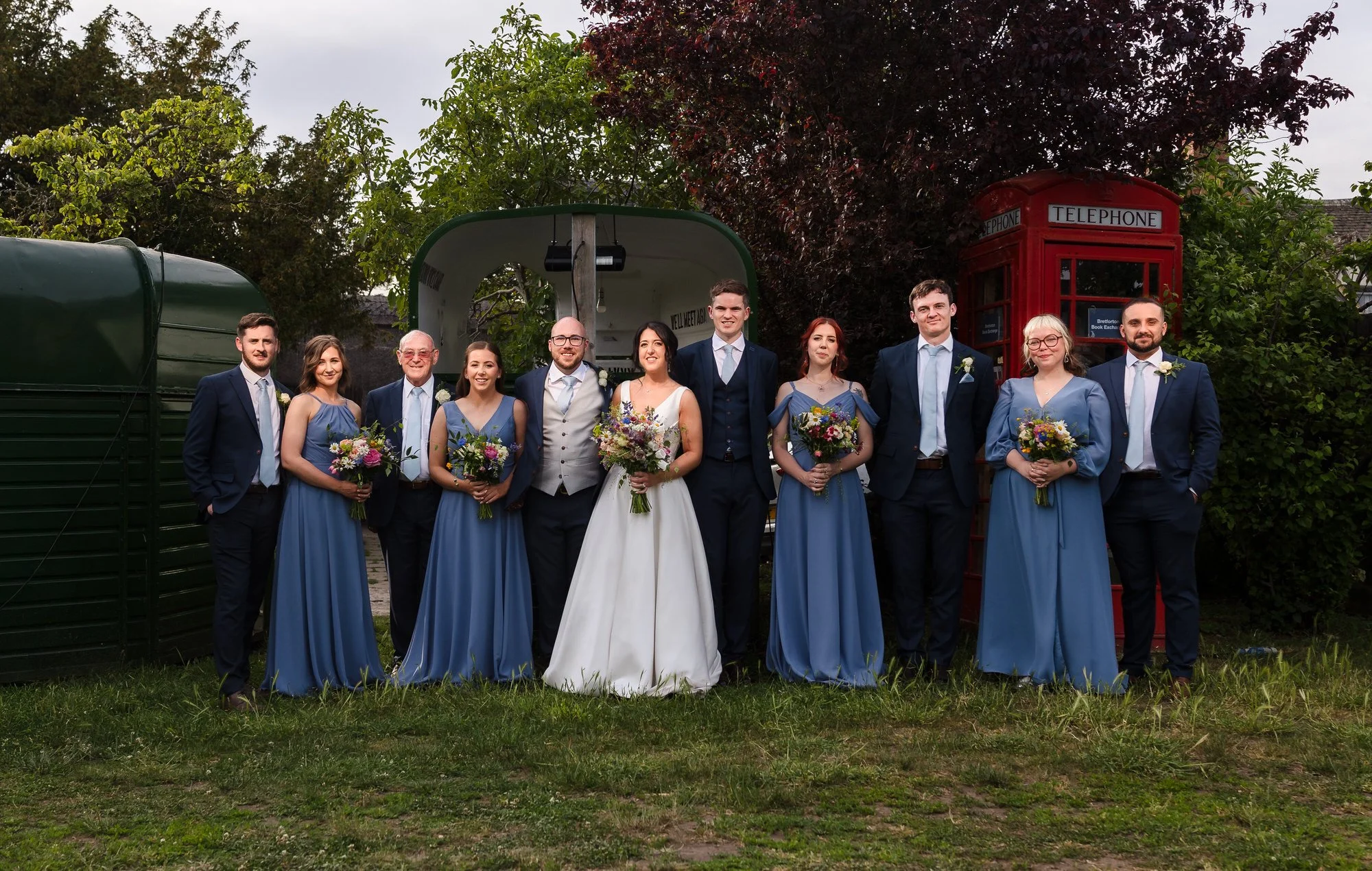 Full wedding party group photo at The Fleece Inn with a red telephone box in the background, Worcestershire wedding venue