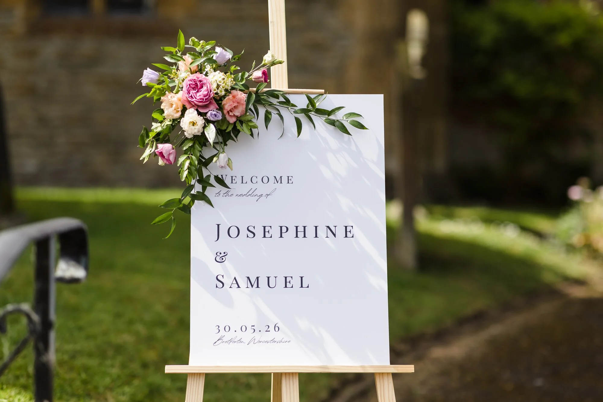 Wedding welcome sign for Josephine and Samuel decorated with florals, outside their Worcestershire ceremony venue