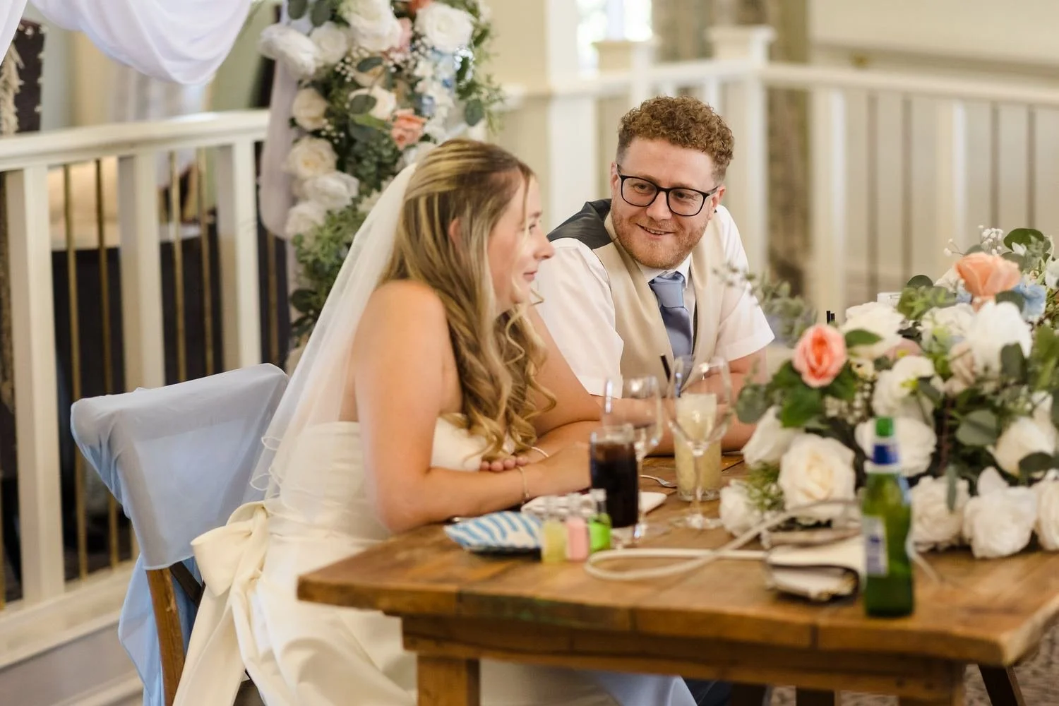 Cheryl and Josh chatting at their flower-filled top table during the wedding breakfast in the Garden Room