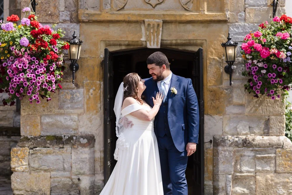 Couple share a moment in the historic doorway at Karma Salford Hall, framed by vibrant hanging baskets.