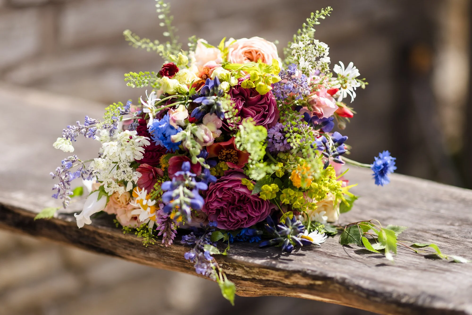 Colourful wildflower bridal bouquet resting on a wooden bench, detail shot from a Worcestershire wedding day