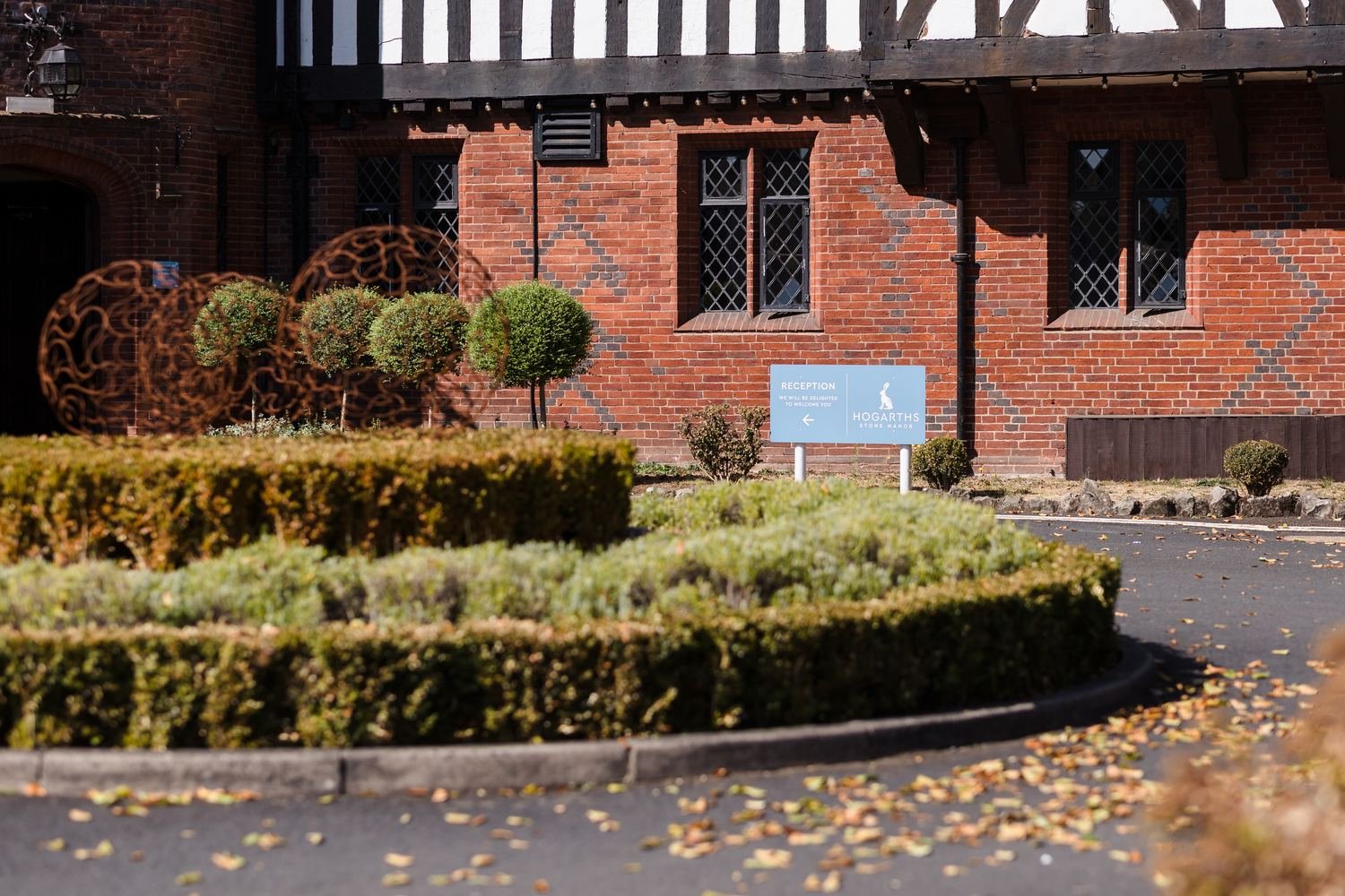 Blue Hogarths Stone Manor reception sign beside clipped hedges and topiary at the front entrance