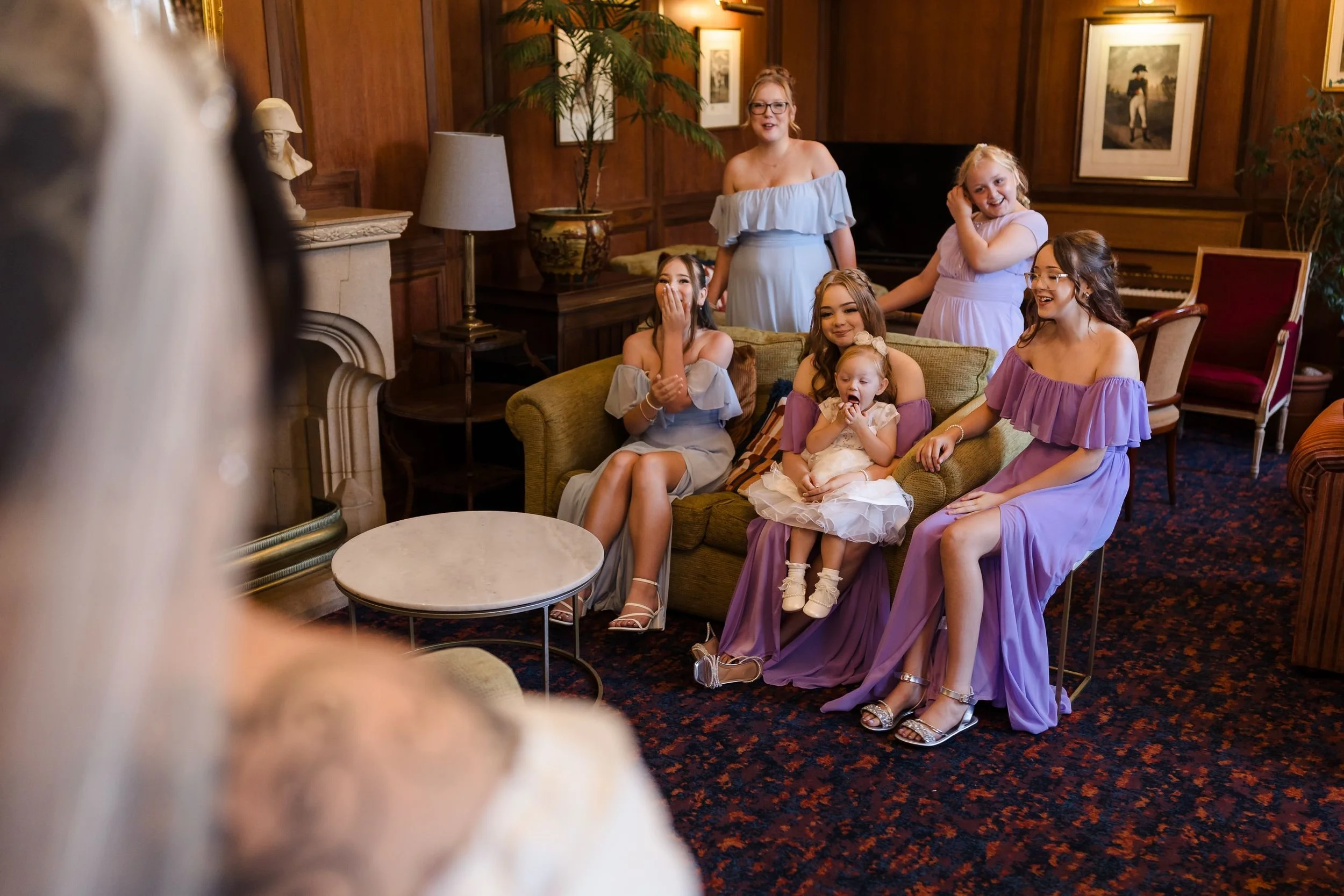 Bridesmaids and a flower girl react to seeing the bride in the library lounge at Berry Head Hotel