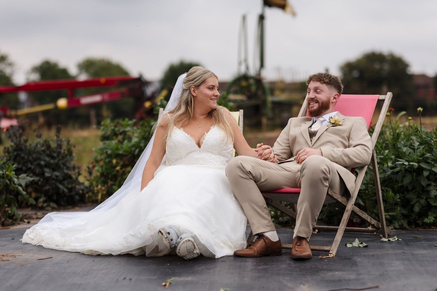 Abbie and Sean holding hands and laughing on a pair of deckchairs, farm machinery behind them