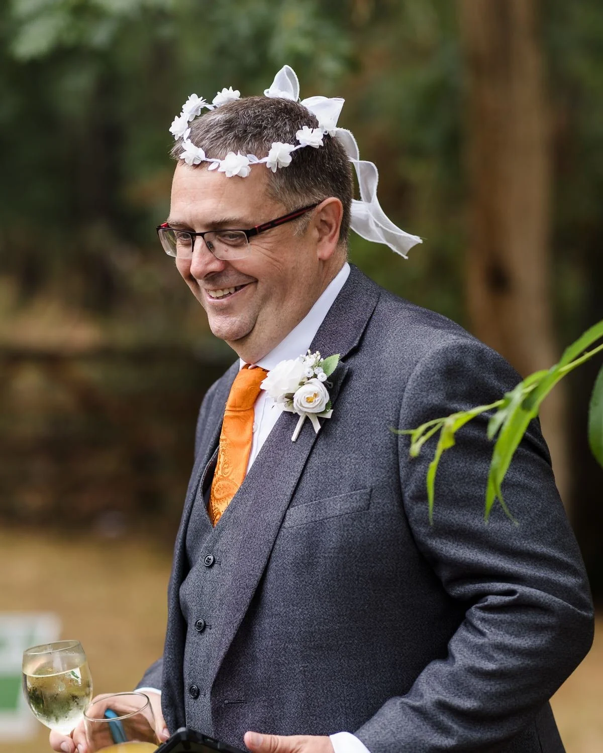 Wedding guest in an orange tie laughing while wearing a white flower crown during the drinks reception