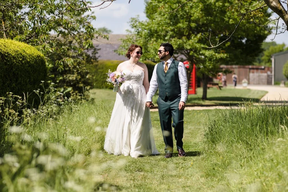Bride and groom walking hand in hand through the grounds at Huntsmill Farm, red telephone box behind.