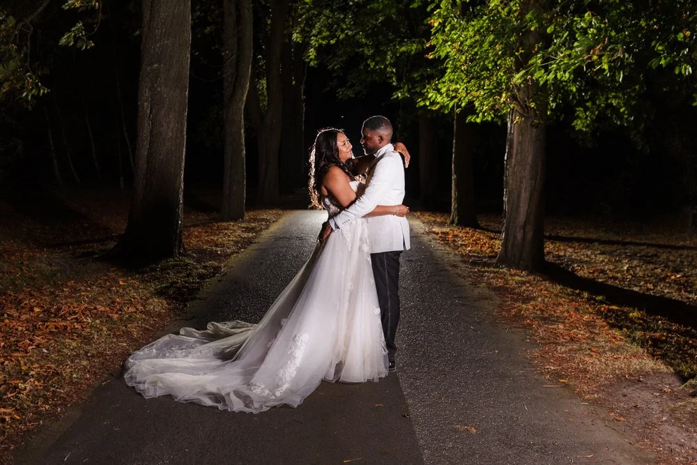 Bride and groom embracing on the tree-lined drive at Hogarths Hotel Solihull, off-camera flash lighting them against the dark avenue.