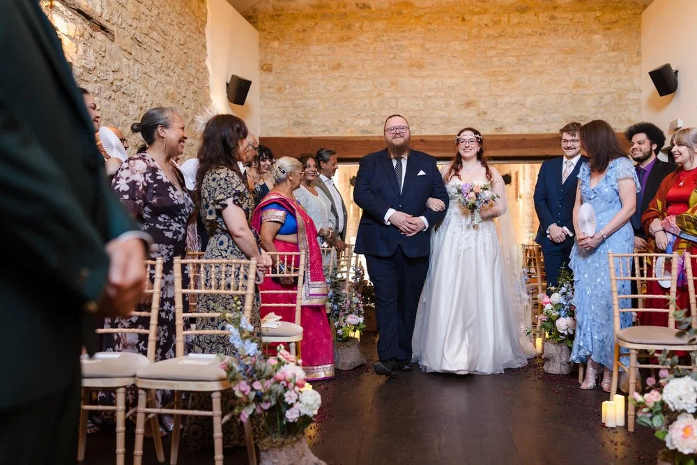 Bride walking down the aisle inside the barn at Huntsmill Farm, guests looking on.