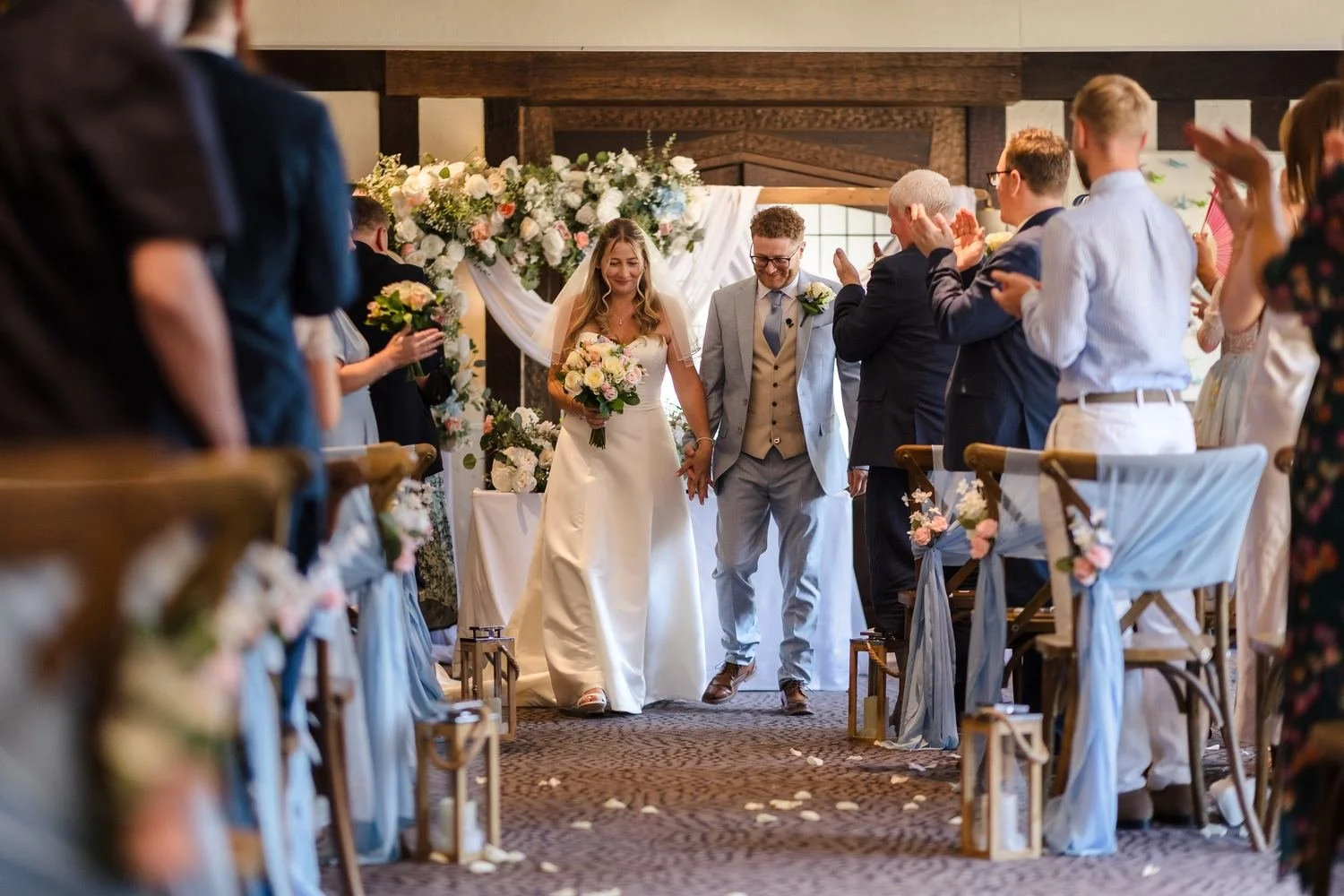Cheryl and Josh walking back down the aisle as guests applaud in the Drawing Room