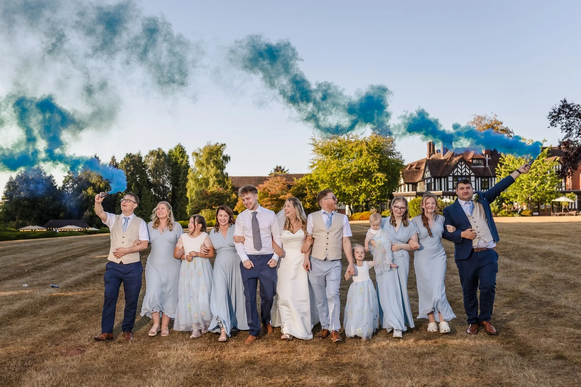 Cheryl, Josh and their bridal party walking arm in arm across the lawn with blue smoke bombs in front of Hogarths Stone Manor