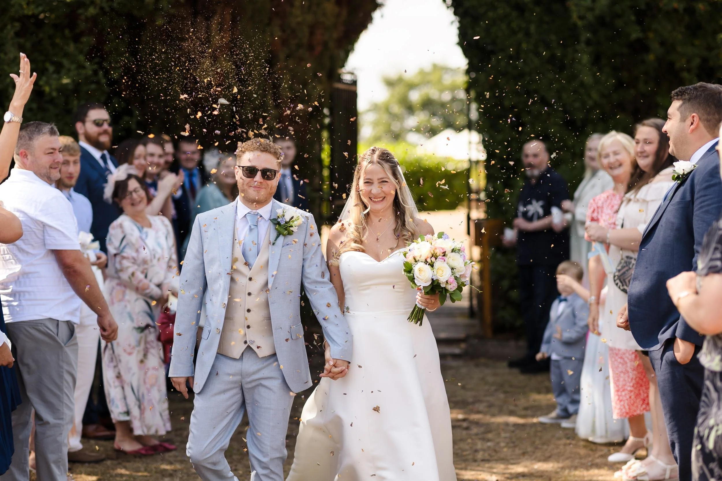 Cheryl and Josh walking hand in hand through a shower of confetti from their guests at Hogarths Stone Manor in Worcestershire