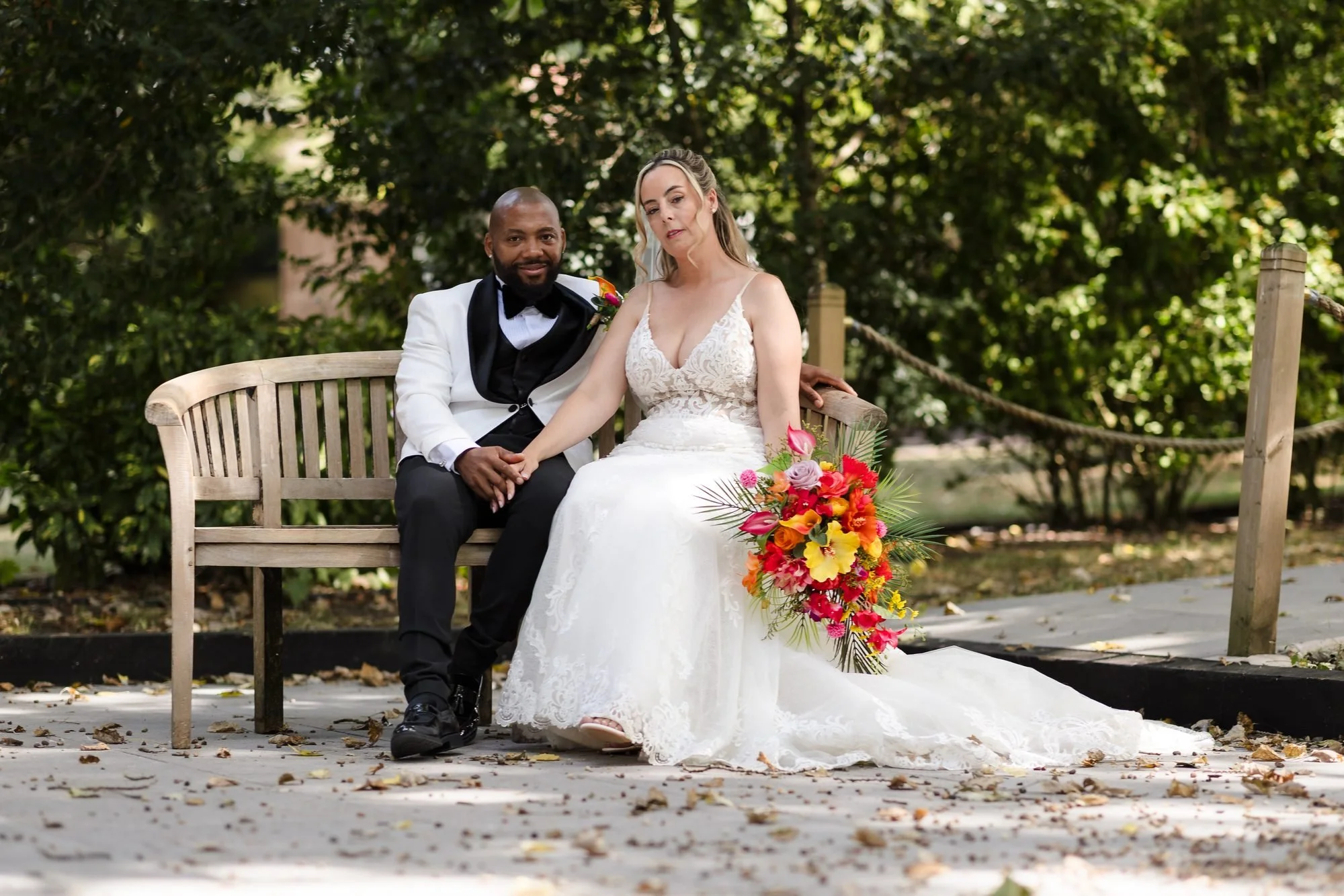 Bride and groom sitting together on a wooden bench in the gardens at Warwick House, Southam