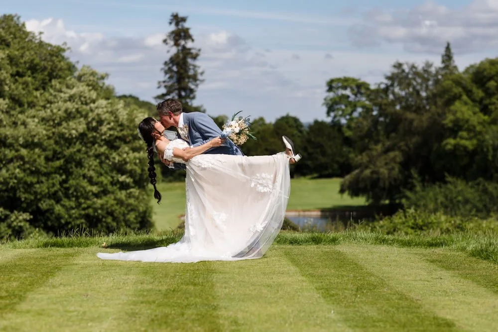Greg dipping Christine for a kiss on the golf course lawn at The Welcombe Hotel, water feature visible behind.