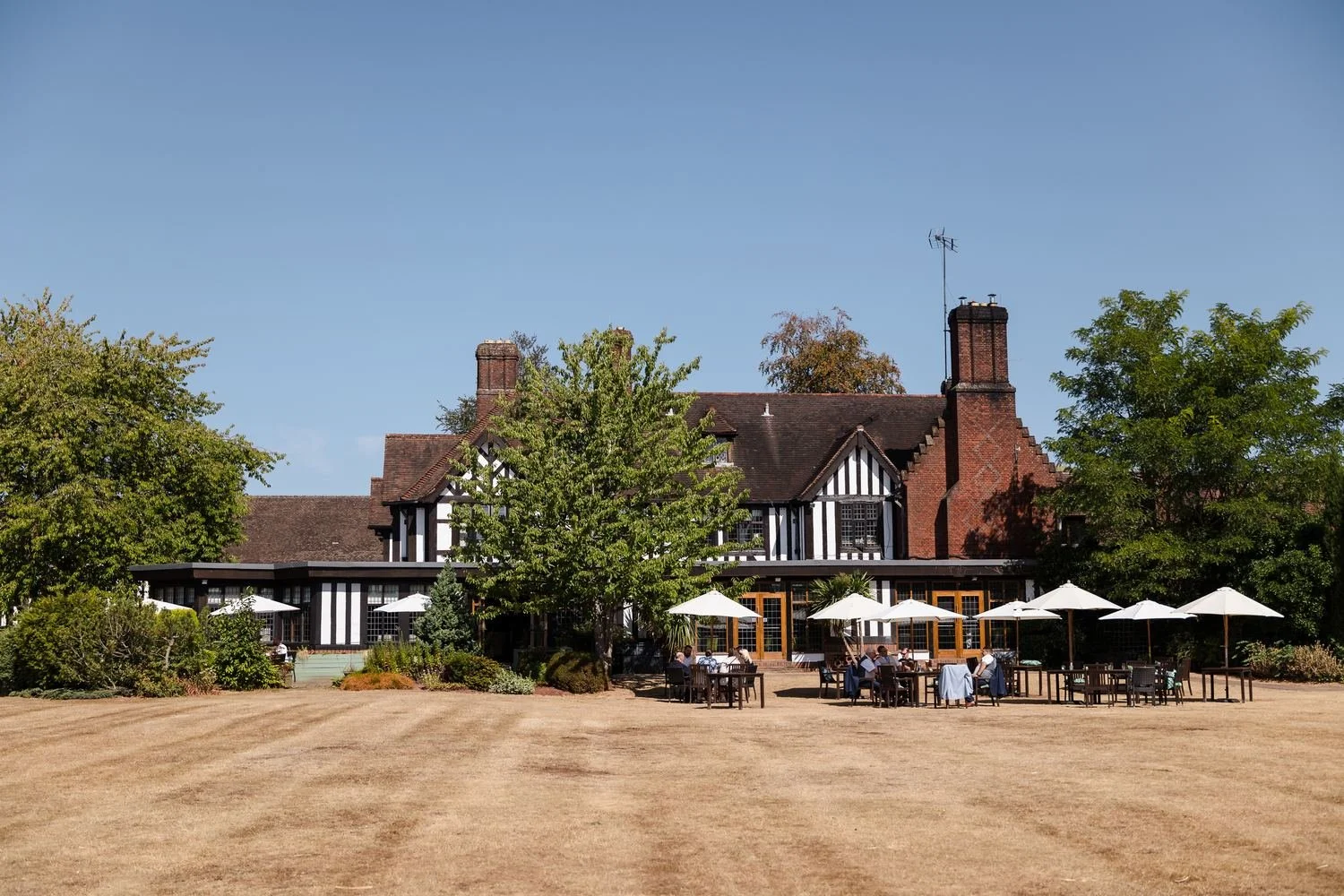 Guests at tables under white parasols on the terrace behind Hogarths Stone Manor on a sunny afternoon