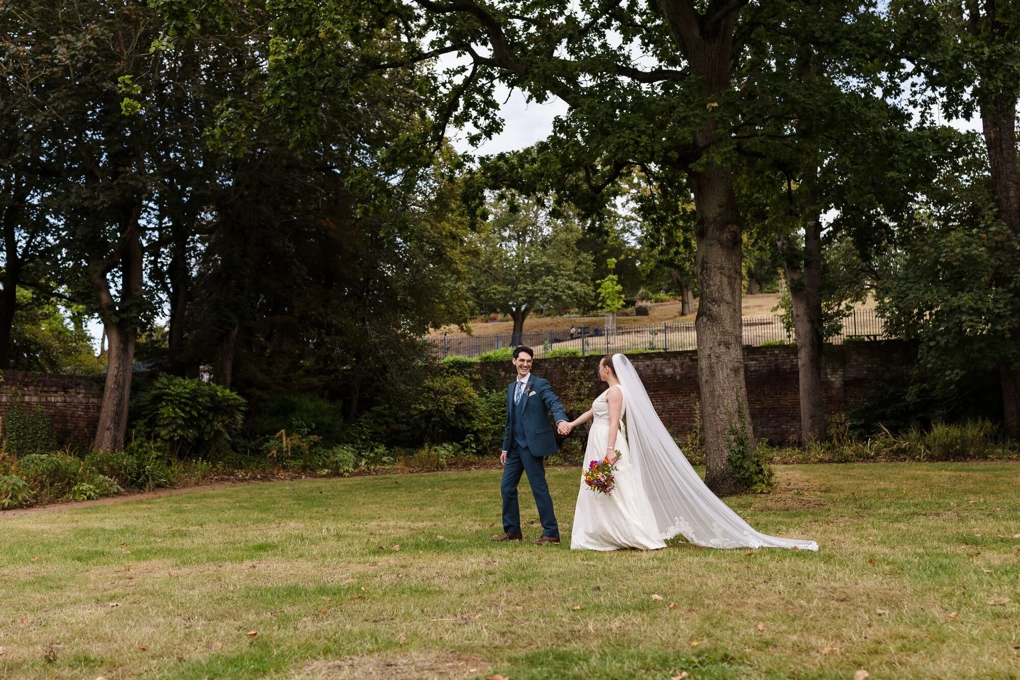 Isabelle and Chris holding hands on the lawn of the walled garden at The Commandery, Worcester, by Once in a Lifetime Photography