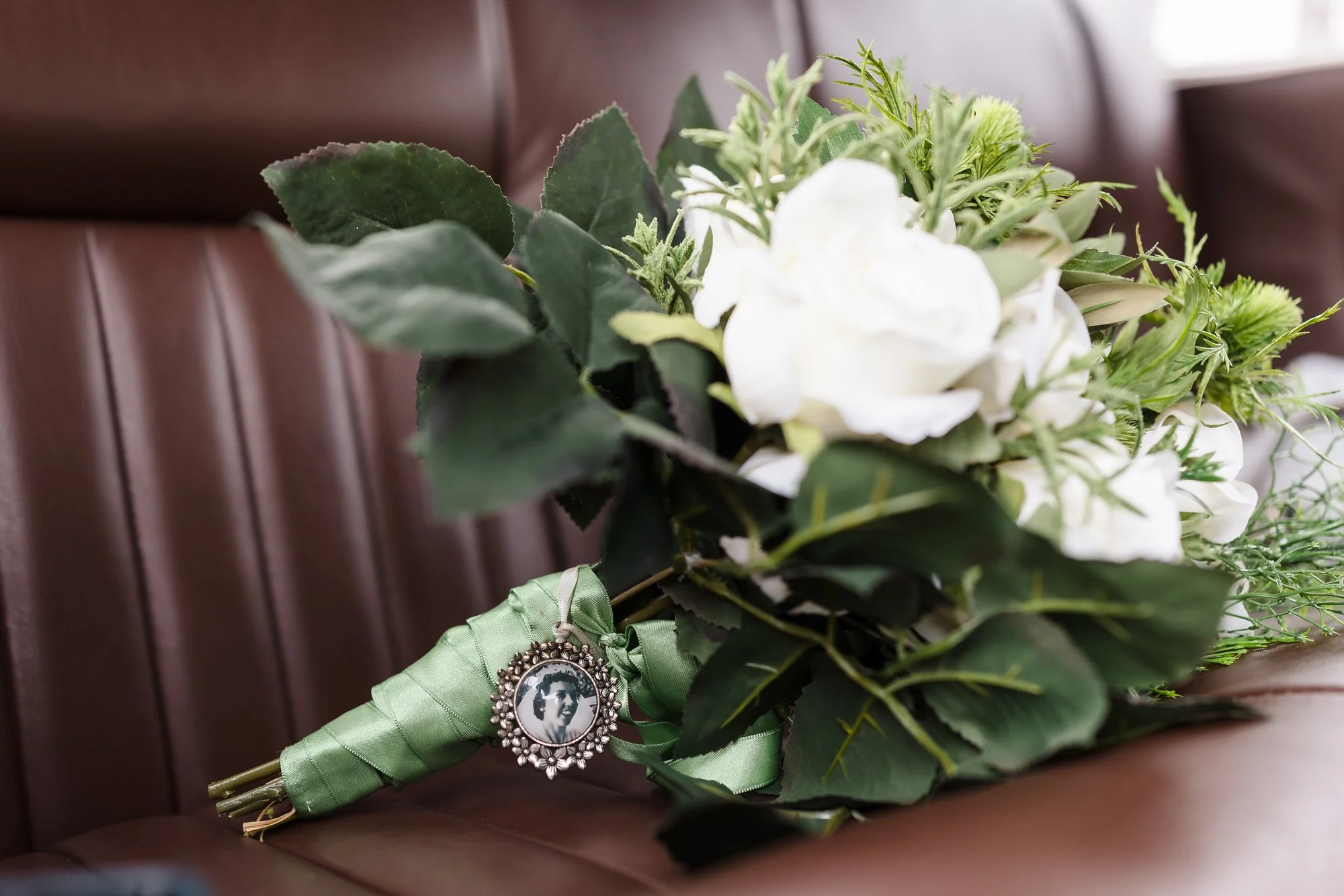 Bride's bouquet with a green ribbon and memorial photo charm, a wedding photography detail from Worcestershire.