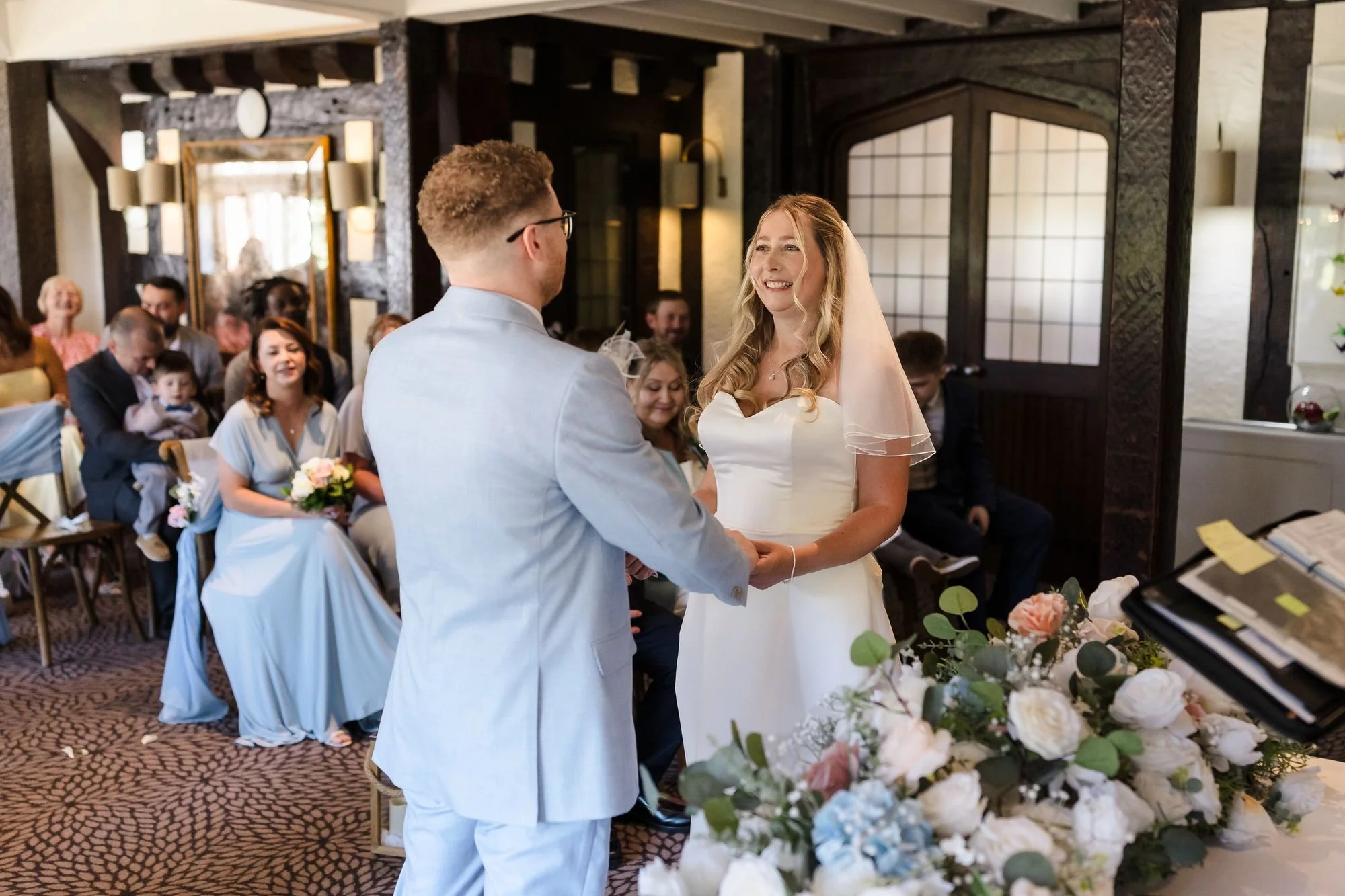 Cheryl smiling at Josh as they exchange vows in the timber-beamed Drawing Room at Hogarths Stone Manor