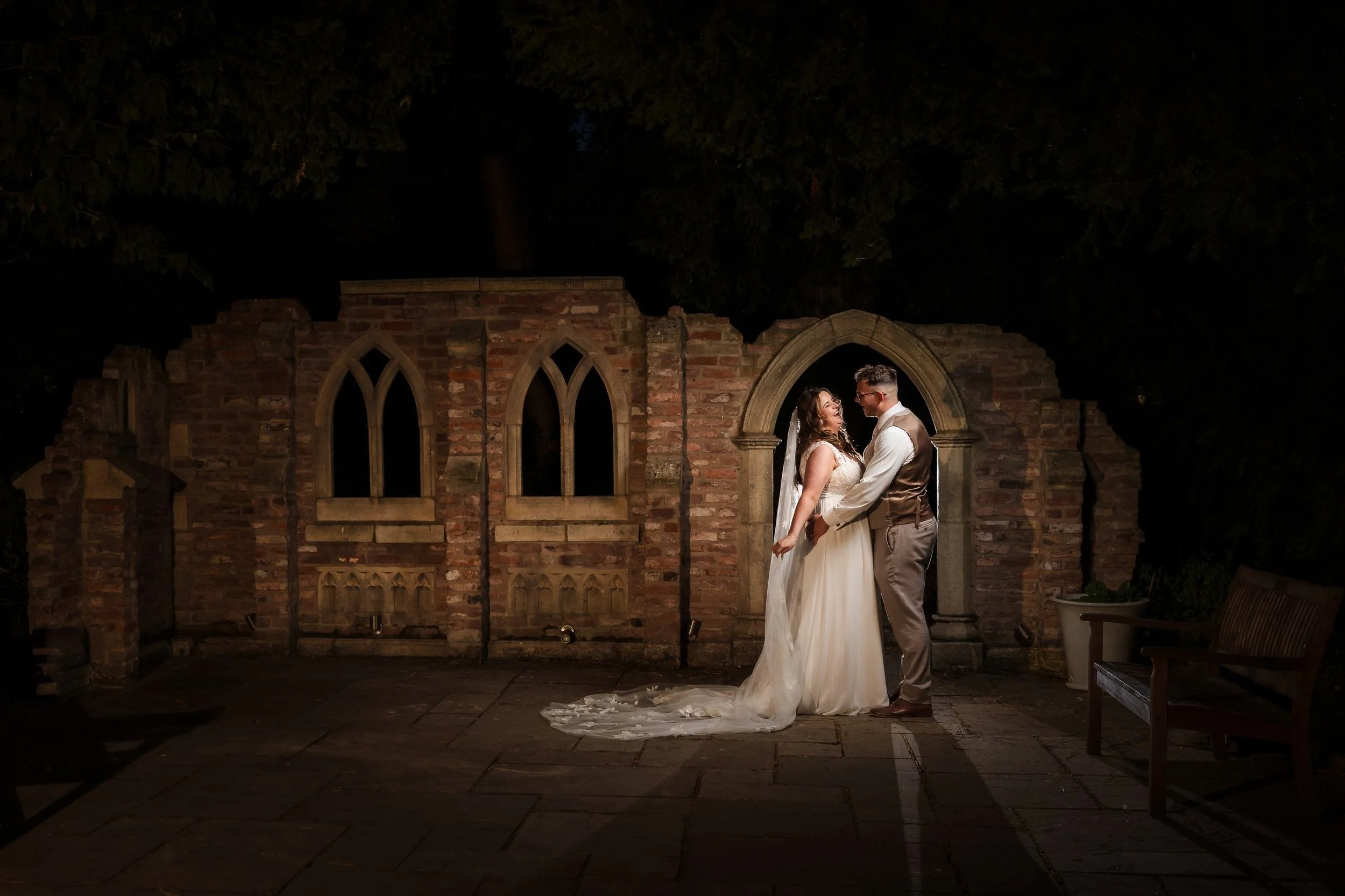 Holly and Dan laughing in the stone archway of the brick ruins at Nailcote Hall at night, lit with warm flash