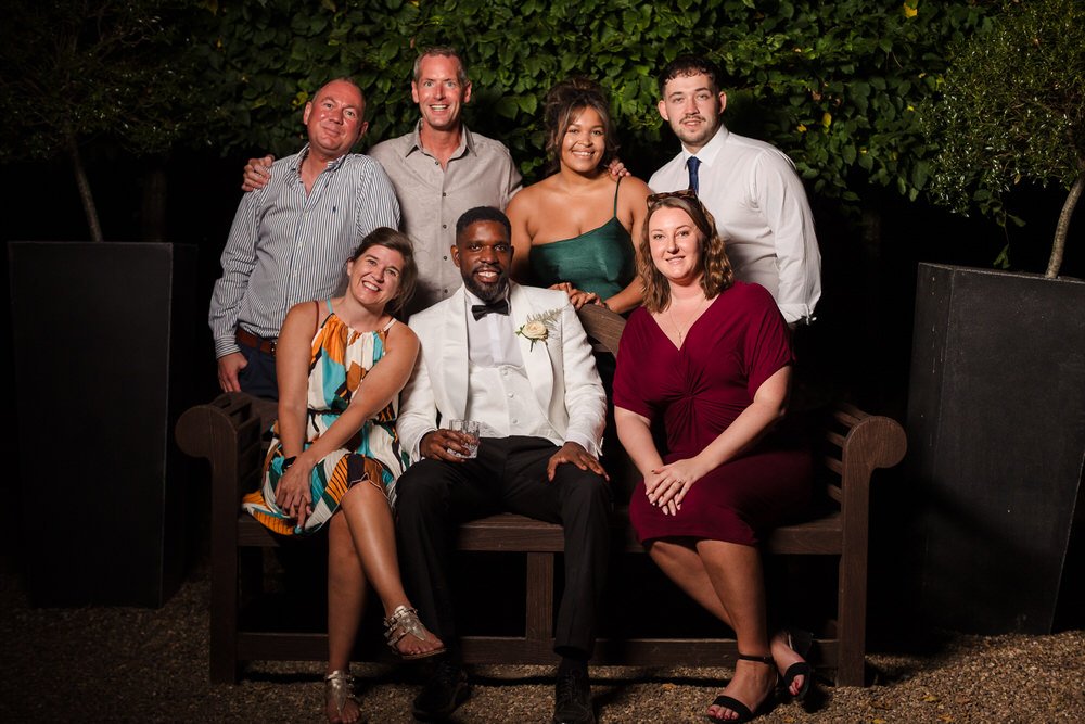 Mike and Sandrine seated with family and friends for a group portrait in the grounds at Hogarths Hotel Solihull.