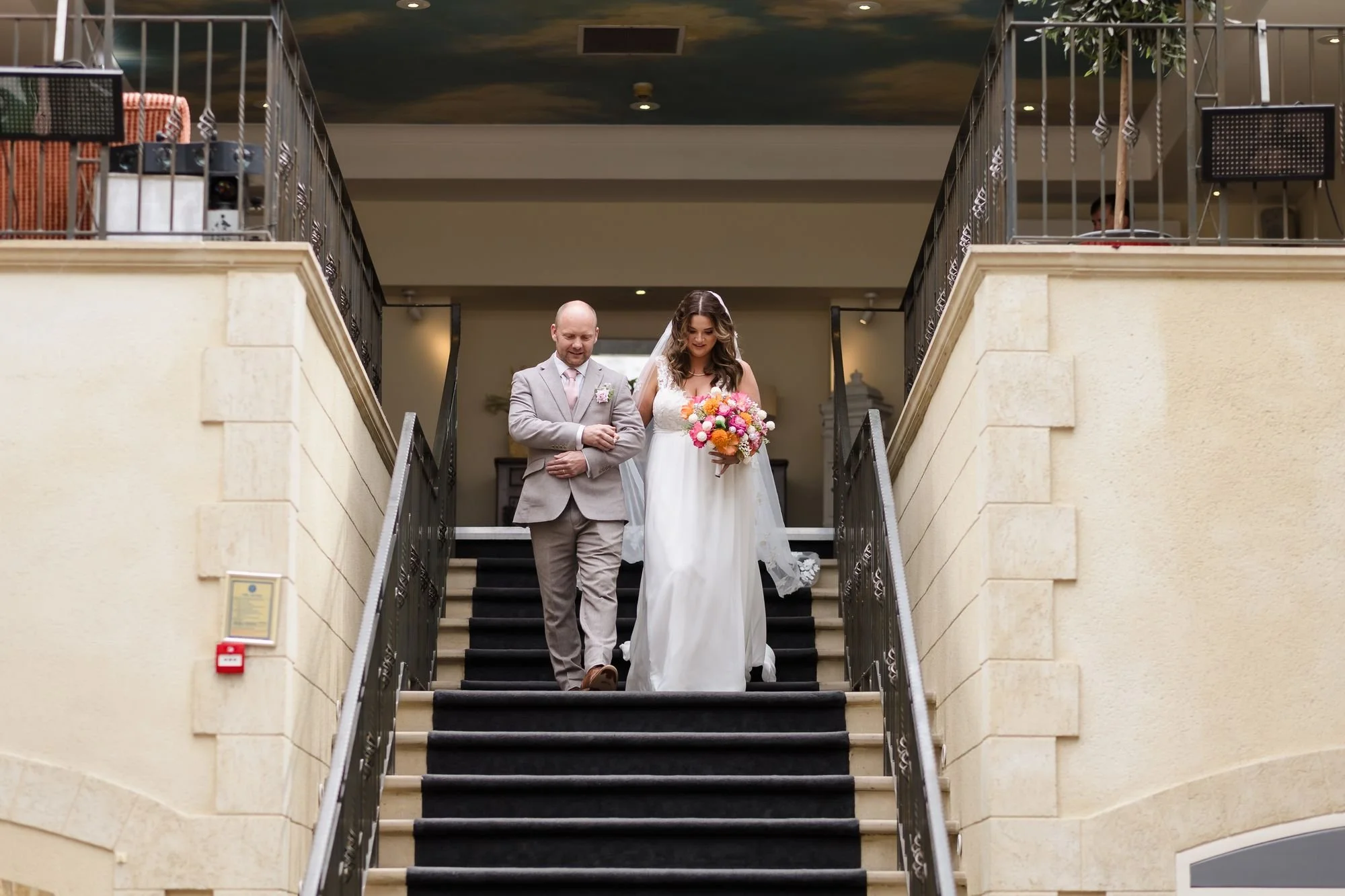 Holly and her dad walking arm in arm down the staircase into the ceremony room at Nailcote Hall