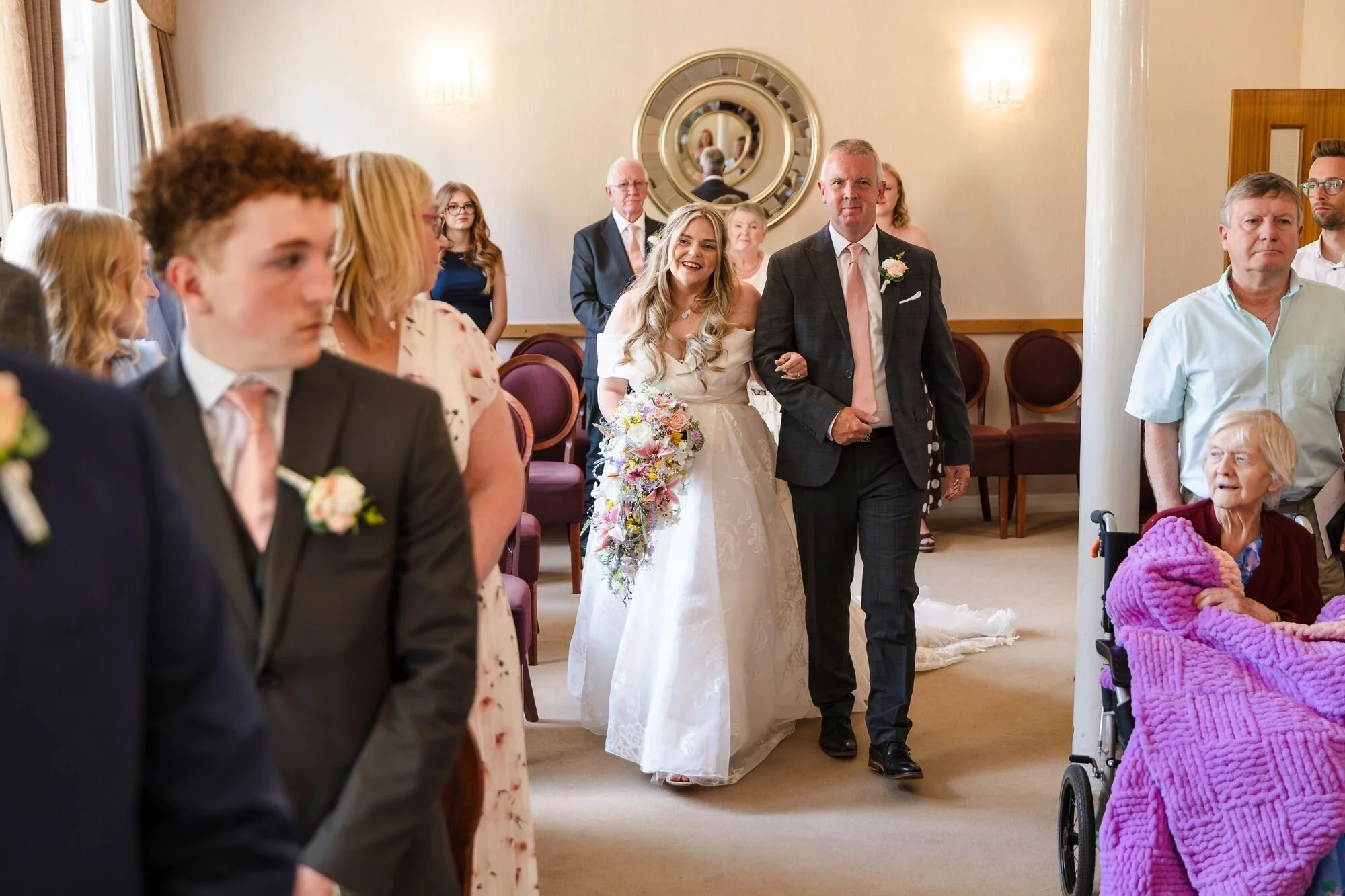 The bride walking in with her father in the ceremony room at Lichfield Registry Office, wedding photography by Once in a Lifetime Photography.