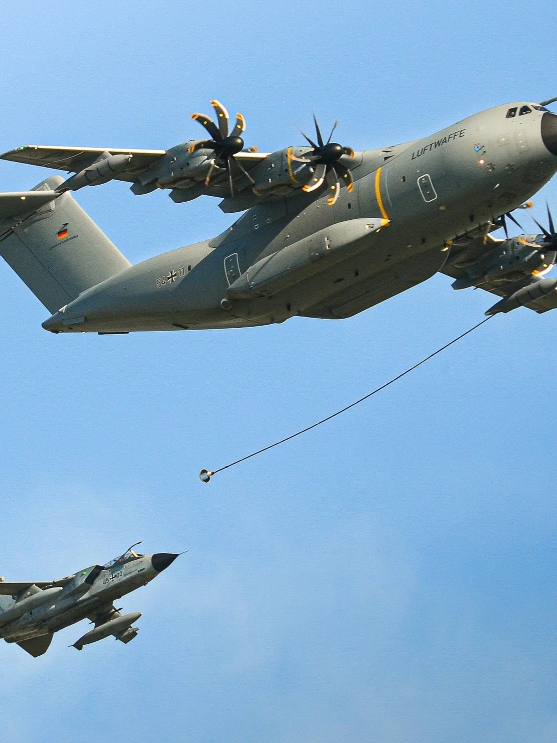 Military aircraft flying in formation with a refueling boom extending from one plane.