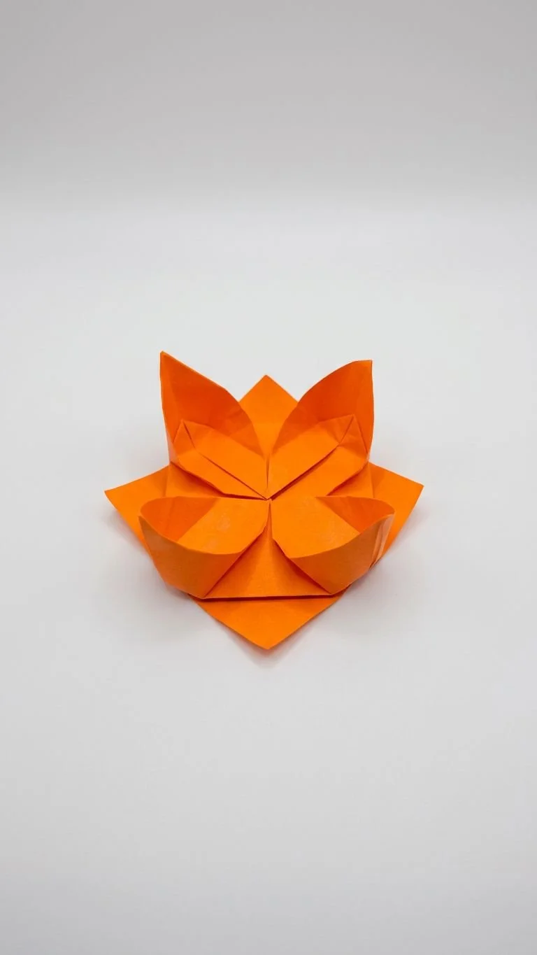 Orange origami butterfly sitting on an orange paper heart, against a plain white background.