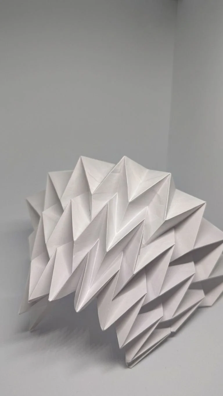 White paper folded into an intricate geometric origami sculpture resting on a gray surface