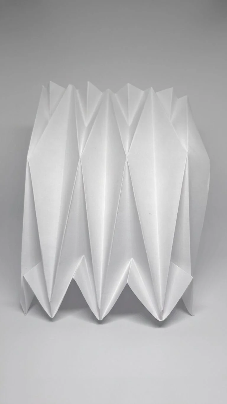 White folded paper art piece on a gray background.