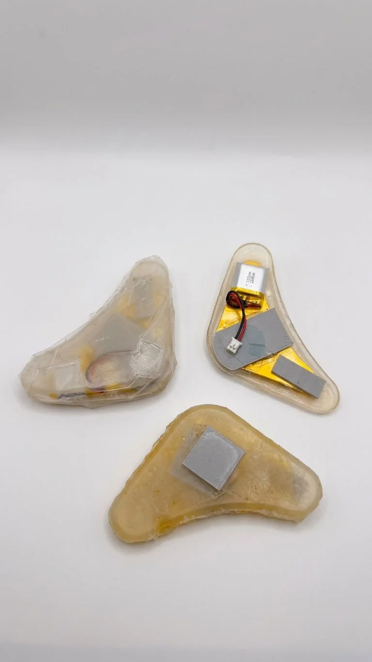 Three small, irregularly shaped objects, possibly medical implants or prosthetics, with electronic components and padding, placed on a white surface.