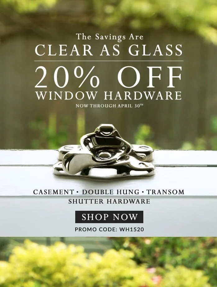 A shiny silver window lock installed on the white wood frame of a window overlooking a garden with out of focus green foliage in the background. 
