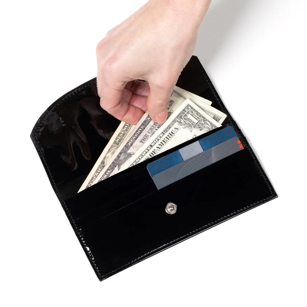 A black vinyl wallet seen from above. A hand reaches in to remove some money. The tops of credit cards can be seen in their respective slots.