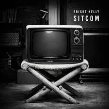 Black and white image of a vintage television on a small wooden foldable table in a room with shelves and a chalkboard in the background. Text on the image reads 'Bright Kelly Sitcom'.