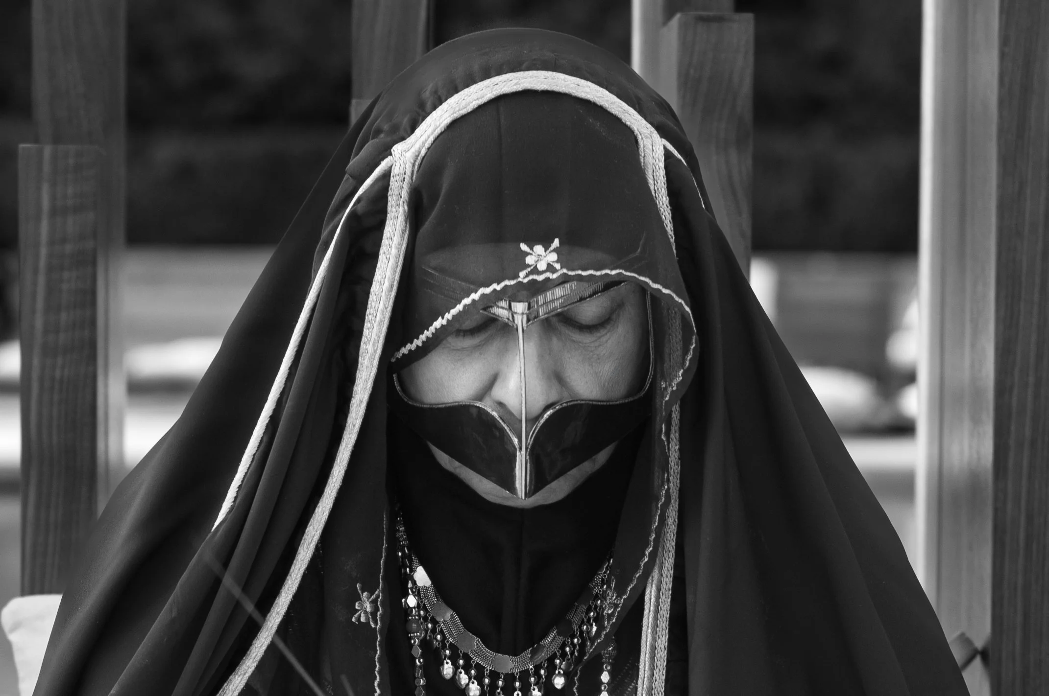 A person wearing a traditional garment and a face mask, with their eyes closed, outdoors.